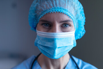 Portrait of caucasian female doctor in hospital wearing face mask, medical cap and scrubs