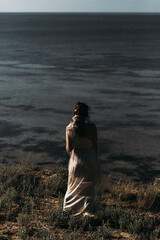 A beautiful girl in a stilted suit stands on a mountain above the sea, a lake on a sunny day.