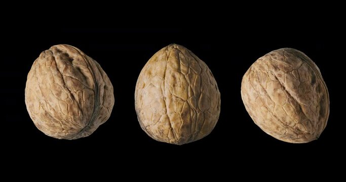 Three walnuts slowly rotate on a black background. 