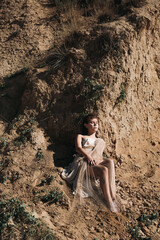 A beautiful girl in a stylized suit sits on a mountain above the sea, lake on a sunny day.