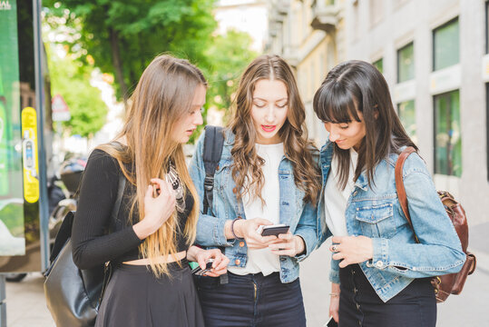 Three young beautiful caucasian women millennials outdoor in the city using smart phone