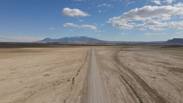Flying drone over empty desert road with snow capped mountain in the distance