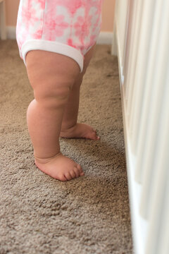 Ten month old toddler holding onto crib rails and standing upright; sturdy baby legs