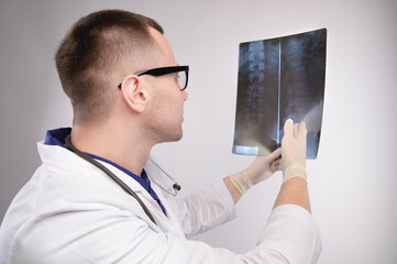male doctor looks and shows at x-rays of the spine, profile portrait, in uniform and glasses. studio photography © yanik88