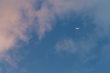 The moon crescent with thin clouds hitting the red light at the sunset, the sky background looks lonely but beautiful. Photo for background