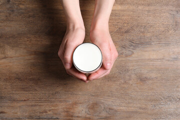 Woman holding glass of milk at wooden table, top view