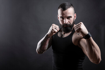Uomo moro muscoloso, tatuato con la barba, stai un posizione di combattimento pronto all'attacco , isolato su sfondo nero
