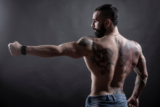 Uomo moro muscoloso e tatuato fa una posa mostrando il braccio e la schiena , isolato su sfondo nero
