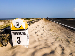 A milestone on the road to the island of Dhanushkodi passing through the sandy dunes off the coast of the town of Rameswaram in Tamil Nadu, India.