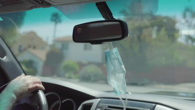 Medical Mask Hanging From Car Rearview Mirror While Driving.