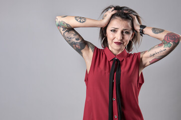 ragazza  mora con i tatuaggi indossa una camicia senza maniche rossa, porta le mani alla testa in...