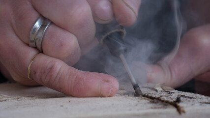 close-up of worker's hand with tools hacking wood with smoke that is seen from overheating of the too