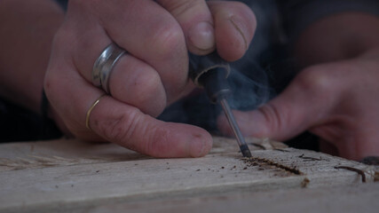 close-up of worker's hand with tools hacking wood with smoke that is seen from overheating of the too