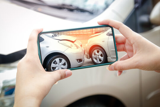 A woman holds a smartphone to take pictures of the area of ​​a car crash in the accident. To collect as evidence of car insurance claim