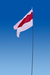 Isolated waving Belarusian national flag on blue sky background. White-red-white flag. A symbol of peaceful protests in Belarus against the dictatorship after presidential elections.