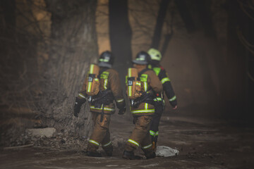 Firefighters put out large massive fire blaze, group of fire men in uniform during fire fighting operation in the city streets, firefighters with the fire engine truck fighting vehicle