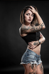 bellissima modella  mora con i tatuaggi e un top nero, posa seria, isolata su sfondo neutro 