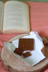 Chocolate bar and open book on a bed. Selective focus.