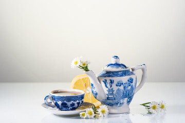 Blue and white teapot, lemon and daisies on white. Copy space