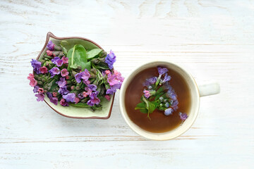 cup of healthy lungwort tea with fresh flowers on table. Medicinal infusion of early wild spring flowers Suffolk lungwort (Pulmonaria obscura). flat lay