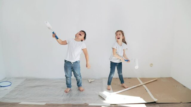 Children paint the wall with a roller Caucasian boy and girl play with rollers Brother and sister repair the house Children have fun Happiness