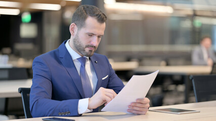 Middle Aged Businessman Reading Documents in Office 