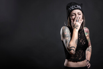 donna con cuffietta nera e  tatuaggi  ride di gusto portandosi la mano alla bocca , isolata su sfondo nero