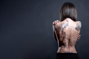 Obraz na płótnie Canvas bellissima ragazza mora con i tatuaggi mostra il la schiena nuda, isolata su sfondo scuro