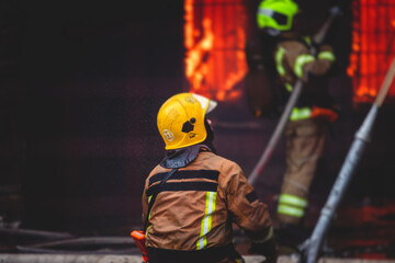 Firefighters put out large massive fire blaze, group of fire men in uniform during fire fighting operation in the city streets, firefighters with the fire engine truck fighting vehicle