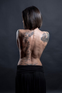 bellissima ragazza  mora con i tatuaggi mostra il la schiena nuda, isolata su sfondo scuro