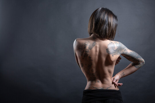 bellissima ragazza  mora con i tatuaggi mostra il la schiena nuda, isolata su sfondo scuro