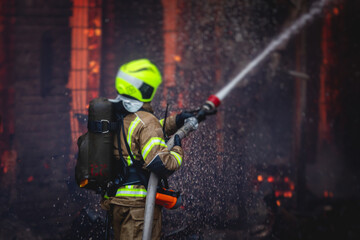 Fototapeta premium Firefighters put out large massive fire blaze, group of fire men in uniform during fire fighting operation in the city streets, firefighters with the fire engine truck fighting vehicle