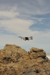 Fototapeta na wymiar A drone hovering with rocks, clouds and blue sky in the background
