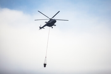 Fire fighting helicopter silhouette with bambi bucket for сarrying water to put out a massive building city fire, process of put out a large blaze bush fire wildifre, aerial firefighting with chopper