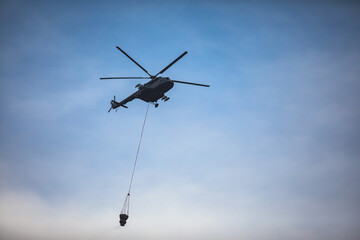 Fire fighting helicopter silhouette with bambi bucket for сarrying water to put out a massive building city fire, process of put out a large blaze bush fire wildifre, aerial firefighting with chopper
