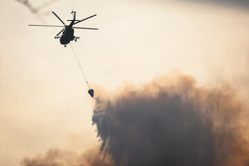 Fire fighting helicopter silhouette with bambi bucket for сarrying water to put out a massive...