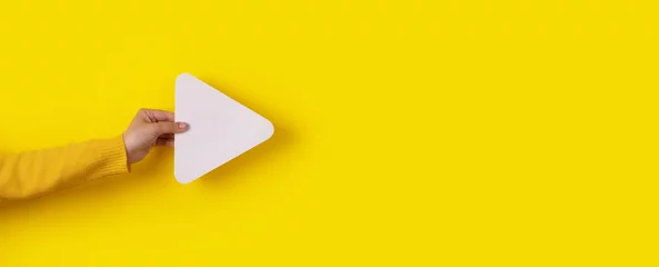 Foto op Plexiglas hand holding media player button icon over trendy yellow background, panoramic layout © alesmunt