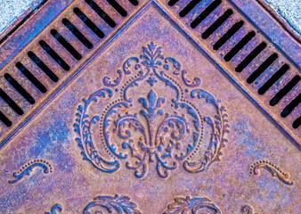 Vintage ornamental metal sidewalk grate - view from above on angle grainy rusted grungy and colorful.
