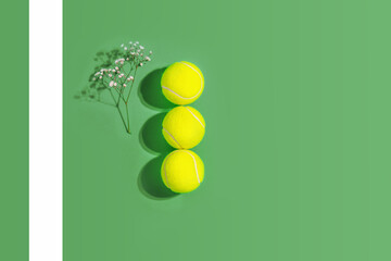 Tennis. Spring sport composition with three yellow tennis balls and flowers on a green background...