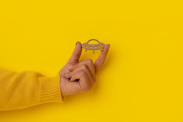 wooden UFO in hand over yellow background