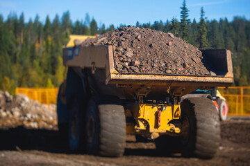 Obraz premium Yellow heavy excavator and dump tip truck tipper excavating sand and working during road works, unloading sand during construction of the new road with workers around