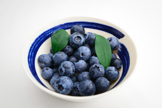 Plate with ripe blueberry on white background. Bowl with ripe blueberry. Water drops on ripe sweet blueberry. Collection of blue and black berries. Conceptual food image. 