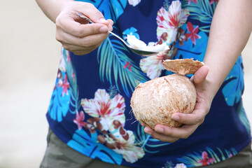 The man's hand held the young coconut in his hand and scooped the coconut meat with a spoon with...