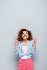 excited woman looking up and pointing with fingers on grey background