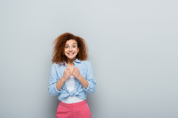 amazed woman showing luck gesture while looking at camera on grey background