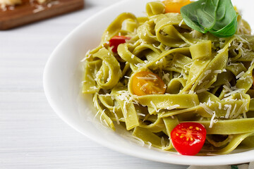 Green pasta with spinach, cherry tomatoes and cheese, on a white table, horizontal, no people,