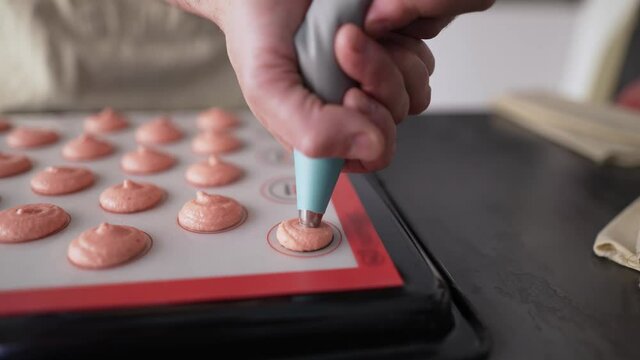 Piping out pink macaron mixture on a slip mat on backing tray