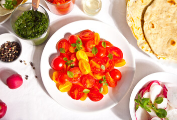 salad of fresh cherry tomatoes with basil on the dinner table with dips, radish salad, pita flat bread