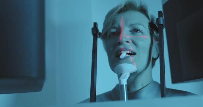 The medical hand is wearing disposable gloves that are rotating a button of the 3D dental tomography (CBCT) scan while a female patient is standing ready for the scanning of her head.