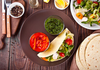 mexican vegan tortilla wrap with vegetables and sauce dips on the dinner table